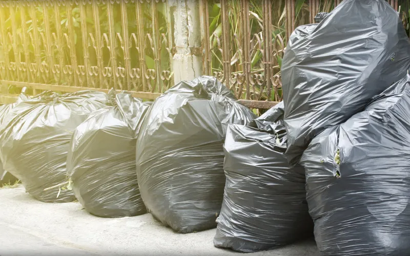 Bags of rubbish stacked by a fence
